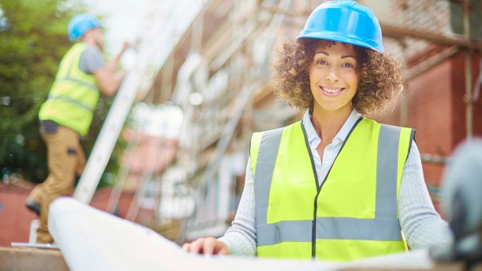 Photo of woman contractor holding blueprints in front of building
